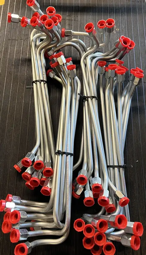 Production batch of identical bent hydraulic tubes bundled with zip ties, all ends capped red